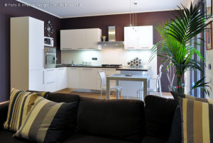 soggiorno living cucina bianca con penisola e parete cacao